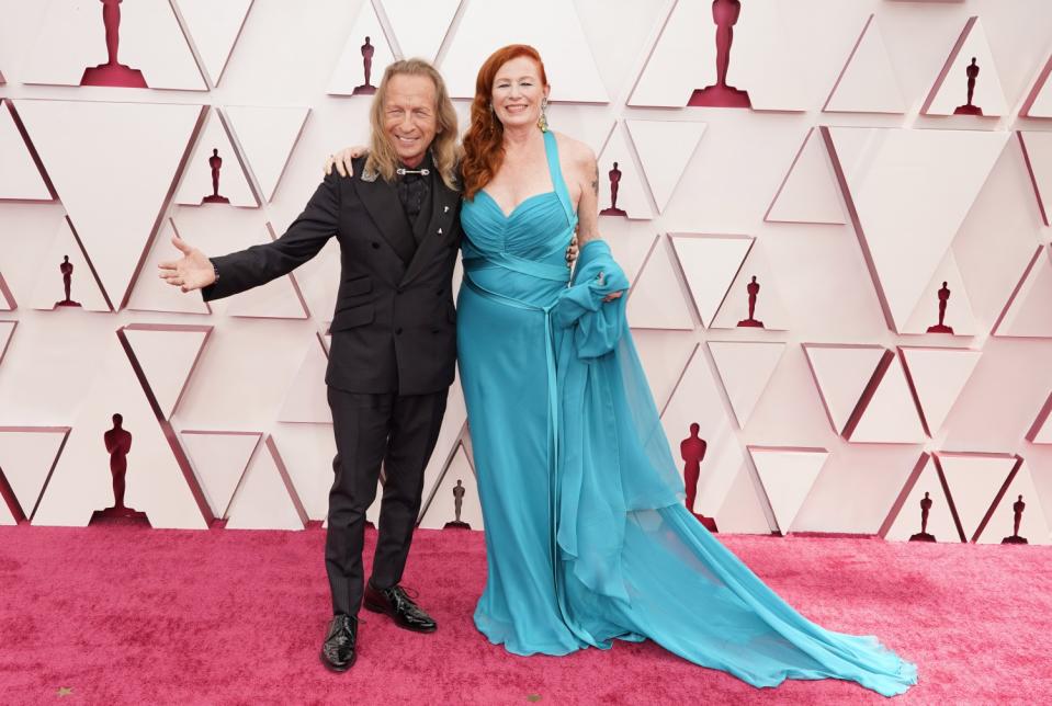 Paul Raci in a black outfit and Liz Hanley Raci in a blue gown with train at the Oscars.