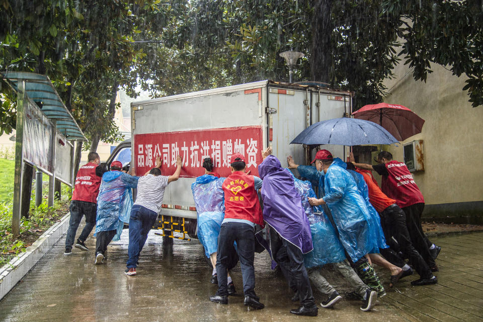 In this photo released by China's Xinhua News Agency, people push a van loaded with disaster relief supplies in Liulin Township of Suixian County in central China's Hubei Province, Friday, Aug. 13, 2021. Flooding in central China continued to cause havoc in both cities and rural areas, with authorities saying Friday that more than 20 people had been killed and another several were missing. (Wu Zhizun/Xinhua via AP)