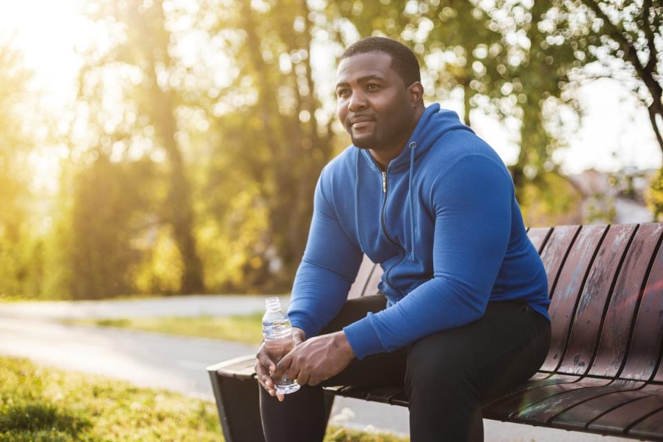 A person sits on a bench with sunshine and nature in the background.