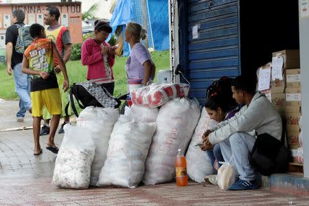 People sit next to bags filled with staple items while they wait for transportation in Pacaraima, Brazil August 3, 2016. REUTERS/William Urdaneta