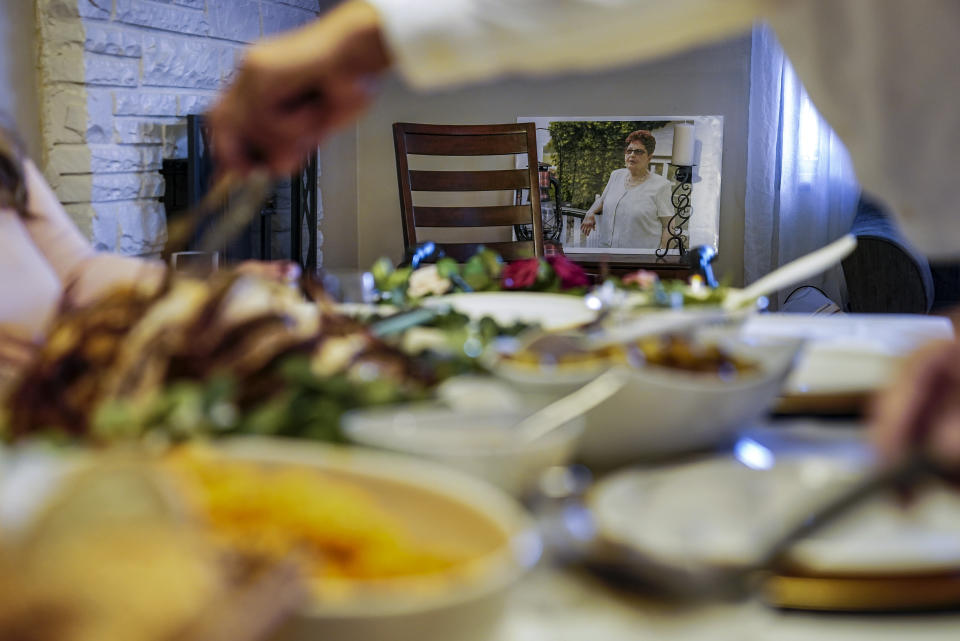 An image Ana Martinez, the recently deceased mother of sisters Vivian Zayas and Alexa Rivera, rests besides an empty chair as Thanksgiving dinner is served, Thursday, Nov. 26, 2020, in Deer Park, N.Y. Ana Martinez died at 78 on April 1 while recovering at a nursing home from a knee replacement. The family is having their traditional meal of turkey, yams, green beans and rice and beans — but Zayas is removing a seat from the table at her home in Deer Park, New York, and putting her mother's walker in its place. (AP Photo/John Minchillo)