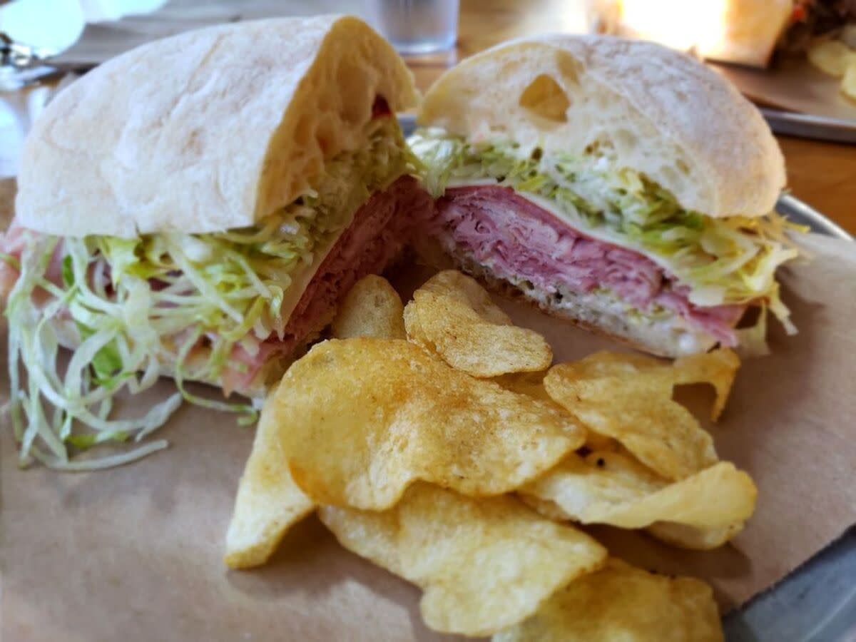 Closeup of Ham and Salami Sandwich with potato chips in the foreground on brown paper, Laurelhurst Market, Portland, Oregon, with a blurred background