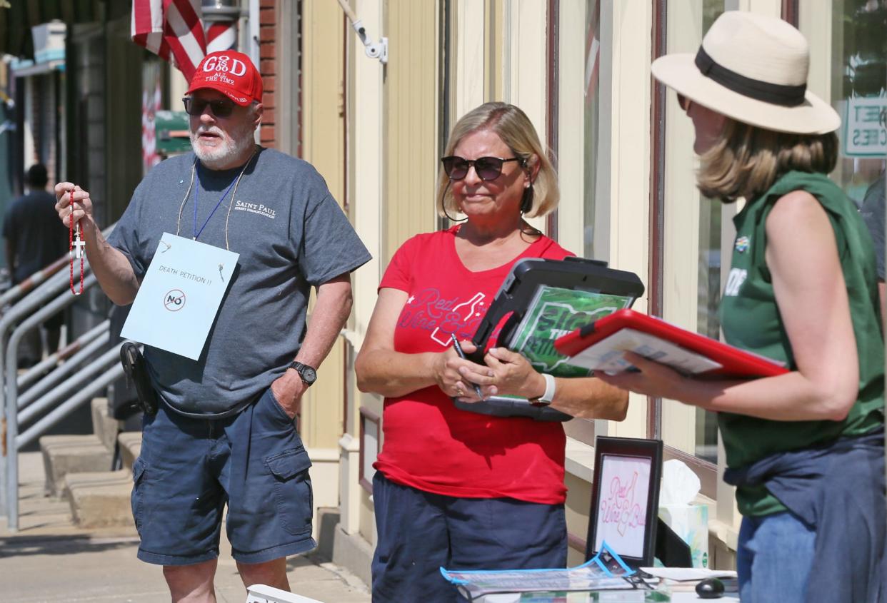 Timothy Garrity prays near volunteers Karen Thorn and Patty Wamsley as they gather signatures for Red Wine & Blue's petition for Ohio's Right To Reproductive Freedom With Protections For Health And Safety outside of Cool Beans in Medina during the summer of 2023. Voters passed the measure, which enshrines abortion as a constitutional right in Ohio. But challengers are not giving up in 2024.