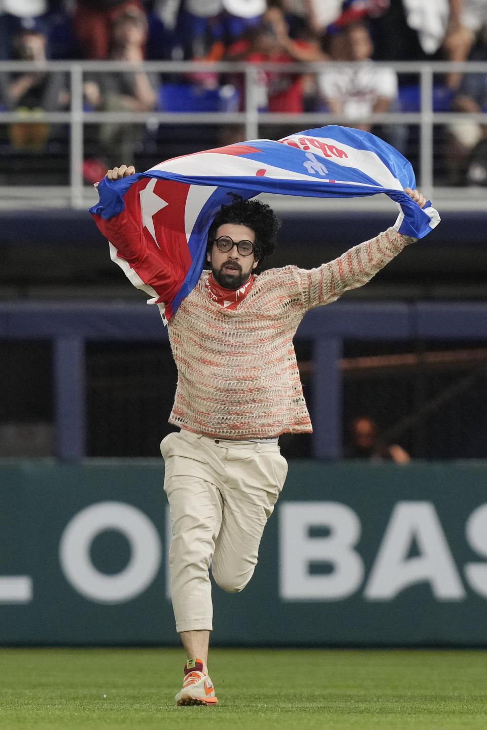 A protestor runs on the field holding a Cuban flag during the eighth inning of a World Baseball Classic game between Cuba and U.S., Sunday, March 19, 2023, in Miami. (AP Photo/Marta Lavandier)
