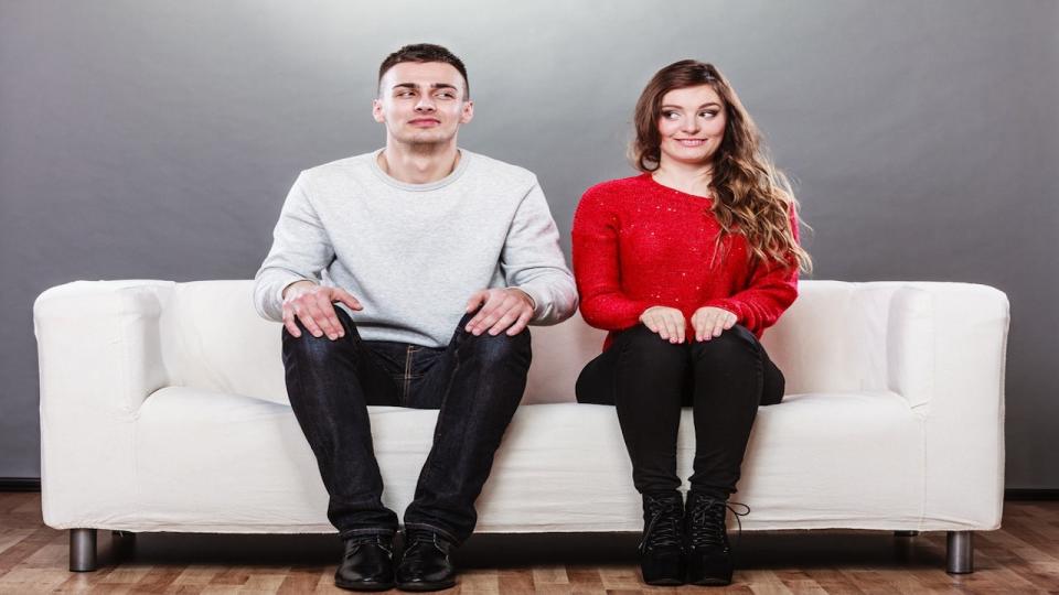Man and woman sitting next to each other on a couch, looking awkward.