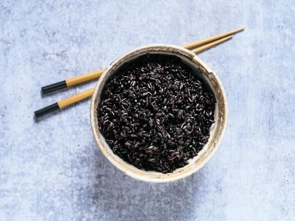 Bowl of black rice with chopsticks on blue background