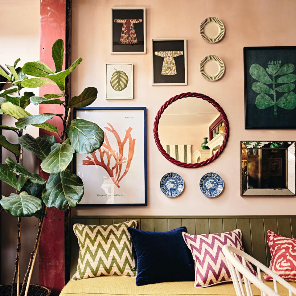 A gallery wall on a pink-painted wall with a sofa and patterned cushions at front