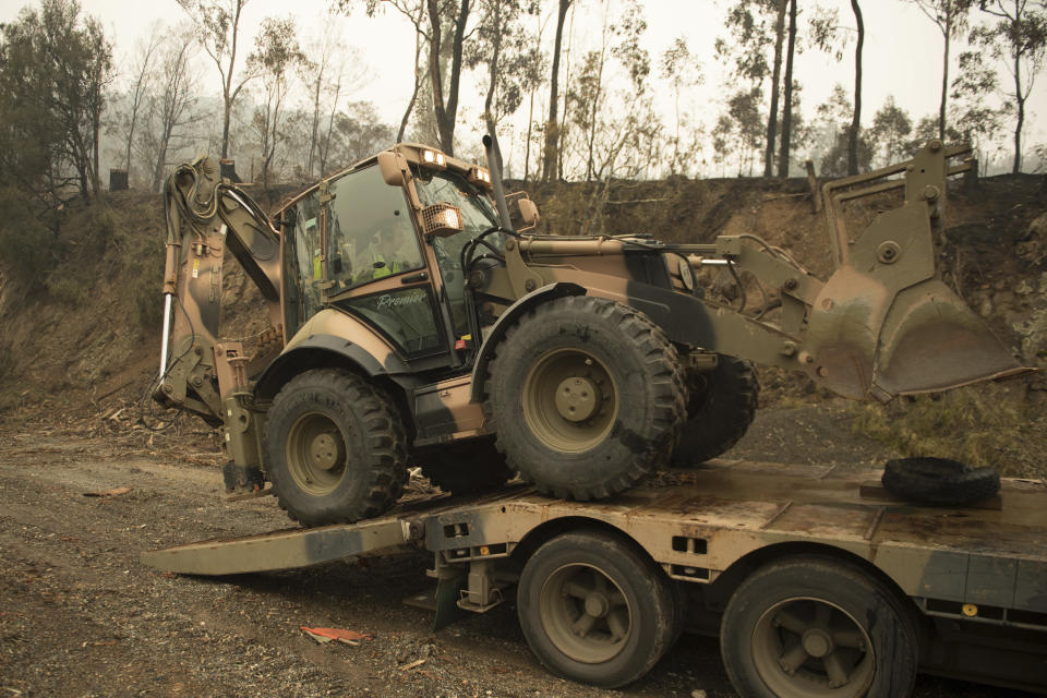 In the image released and dated Monday, Jan. 6, 2020, by the Australian Department of Defence, plant operators Cpl. Duncan Keith and Sapper Ian Larner of the 22nd Engineer Regiment use a 434 backhoe to assist staff from Forestry Management Victoria to clear fire damaged trees from the great Alpine road between Bairnsdale and Omeo during Operation Bushfire Assist 19-20 in Bairnsdale, Victoria, Australia. Australia's government on Monday said it was willing to pay “whatever it takes” to help communities recover from deadly wildfires that have ravaged the country. (Australia Department of Defence via AP)