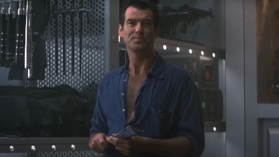 Pierce Brosnan smiles, as he holds a dart fan, in Tomorrow Never Dies.