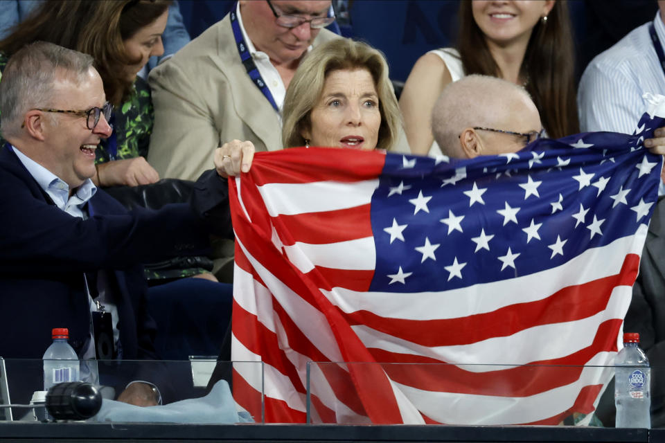 The U.S. ambassador to Australia Caroline Kennedy holds up her national flag as Australian Prime Minister Anthony Albanese watches during the semifinal between Tommy Paul of the U.S. and Novak Djokovic of Serbia at the Australian Open tennis championship in Melbourne, Australia, Friday, Jan. 27, 2023. (AP Photo/Asanka Brendon Ratnayake)