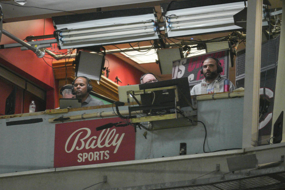 FILE - Cincinnati Reds' Joey Votto, right, sits in the broadcast booth with John Sadak, center right, and Barry Larkin, center left, during a baseball game against the St. Louis Cardinals Wednesday, Aug. 31, 2022, in Cincinnati. Amazon will partner with the Diamond Sports as part of a restructuring agreement as the largest owner of regional sports networks looks to emerge from bankruptcy. Diamond owns 18 networks under the Bally Sports banner. Those networks have the rights to 37 professional teams — 11 baseball, 15 NBA and 11 NHL.(AP Photo/Jeff Dean, File)