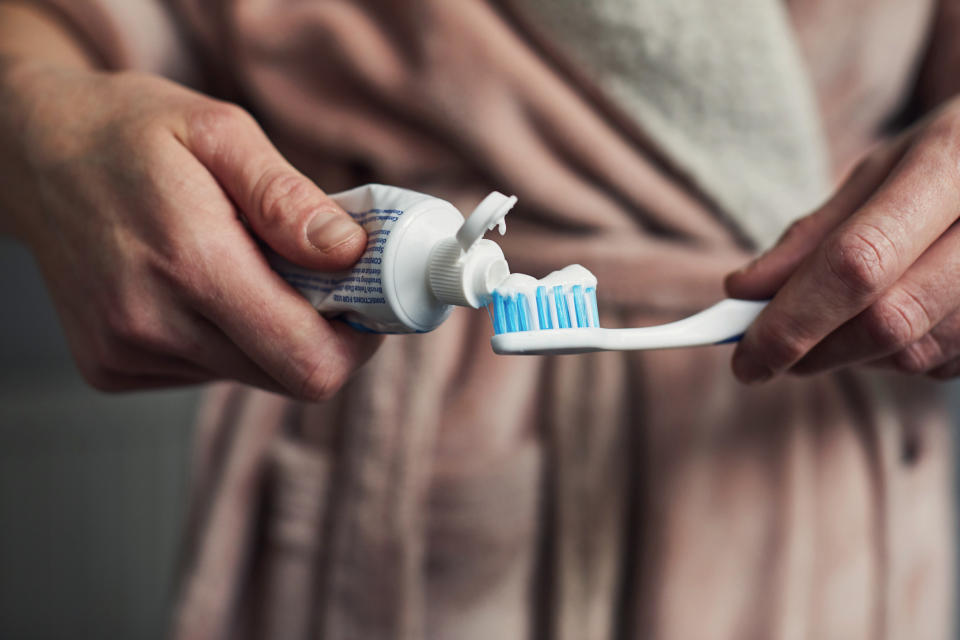 Person wearing a robe squeezing toothpaste onto a toothbrush