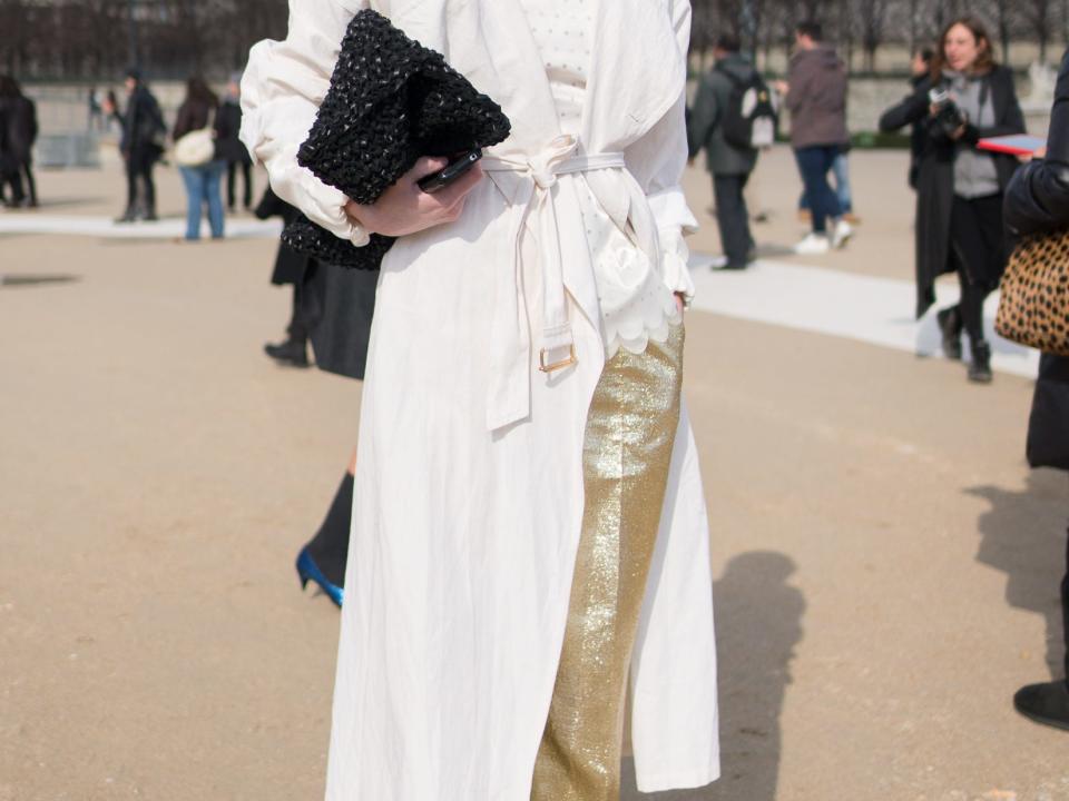 person wearing white trench coat over gold sparkly pants and black heels