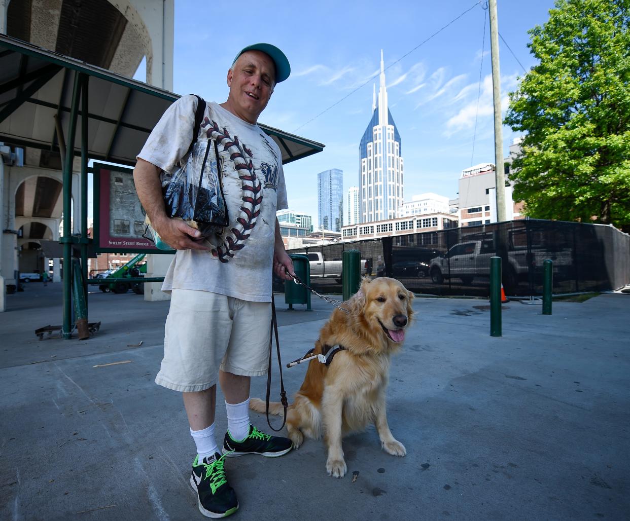 Scott Hegle and his guide dog, Lumiere, stand under the Pedestrian Bridge during the CMA Fest in Nashville, Tenn., Saturday, June 11, 2022.