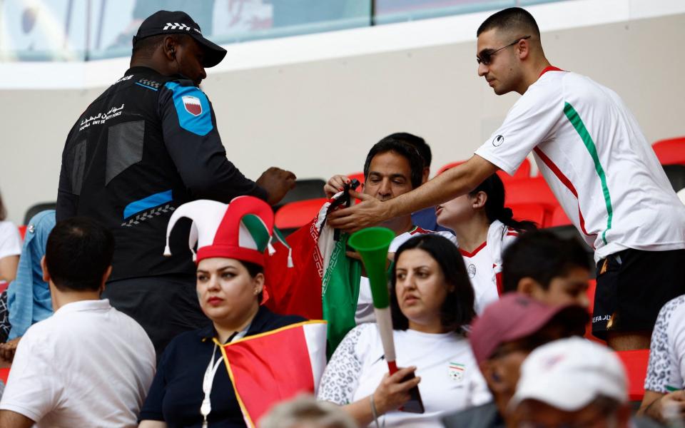 A police officer inspects Iran flags covered with a cross held by Iran fans inside the stadium - Reuters