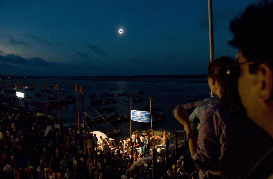 a total solar eclipse unfolds, plunging the ganges river into darkness with people watching on.