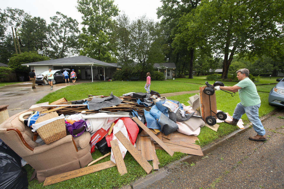 Homeowner Stephen Punkay, right, dumps a cart-load of wet carpet to add to the debris pile, after the Baker Drive home that he and wife Amy share with their six children got at least six inches of water in Monday night's deluge of rain in the Westminster subdivision, as they clean up with the help of family, neighbors and "church family" from Community Bible Church, on Tuesday, May 18, 2021, in Baton Rouge, La. Heavy rains have swept across southern Louisiana, flooding homes, swamping cars and closing a major interstate. (Travis Spradling/The Advocate via AP)