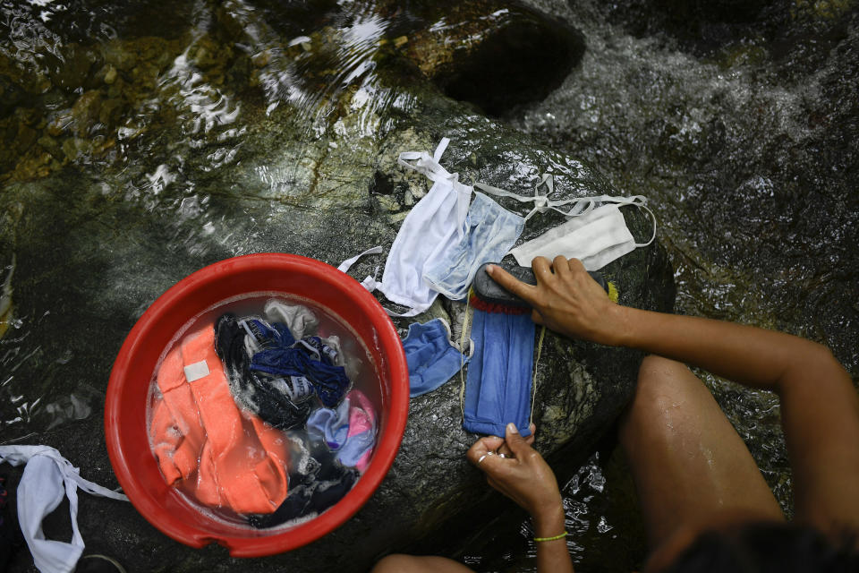 A woman scrubs her protective face masks with runoff water from the Avila mountain in Caracas, Venezuela, Sunday, June 21, 2020. Venezuela's water crisis is nothing new, but water today is even more important due to the new coronavirus crisis pandemic. (AP Photo/Matias Delacroix)