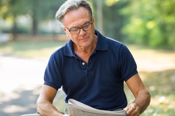 Older man reading a newspaper outdoors