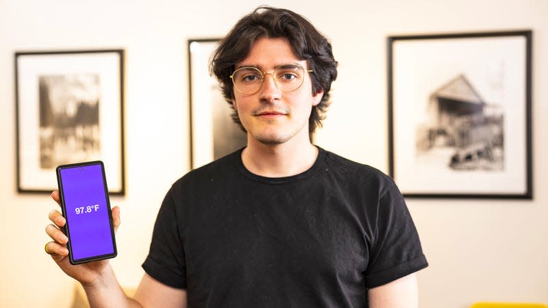 Lead author Joseph Breda holding a smartphone running the FeverPhone app showing a temperature reading on screen.