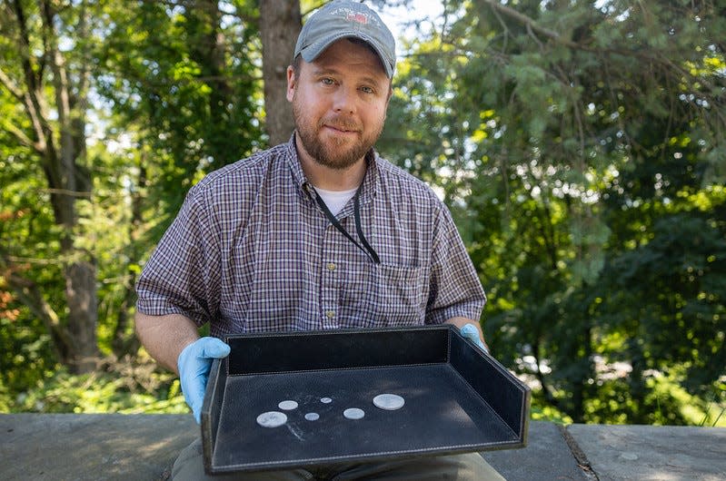 Paul Hudson, West Point's archaeologist, displays the artifacts found in the dried silt of a time capsule opened on Aug. 28, 2023. The unsealing ceremony seemed to end in disappointment, but further digging revealed the six coins and a commemorative medal.