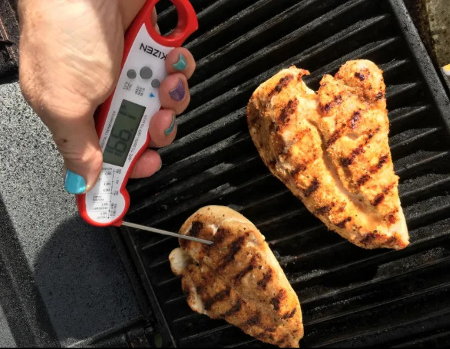 someone reading the temperature of chicken on a grill using the digital thermometer