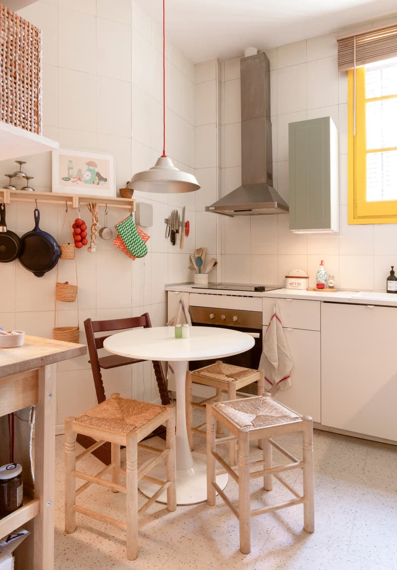 White kitchen with small round table and stools, white tile walls, and shelf with pots and pans hanging