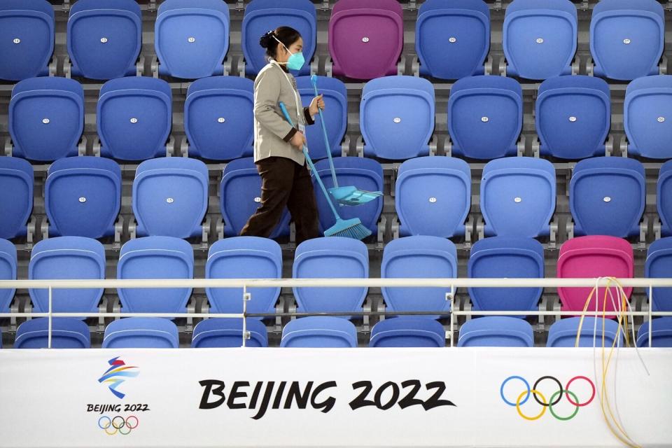 A maintenance worker wearing a face mask walks through an empty section of spectator stands at the skating oval.