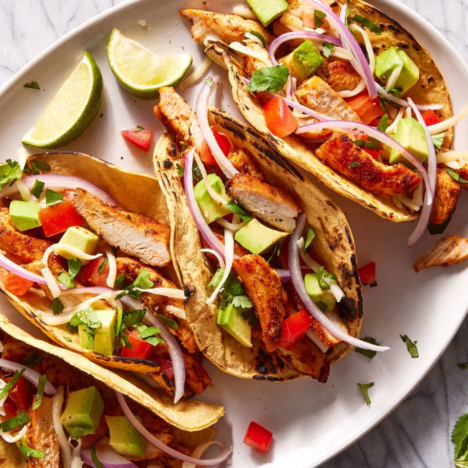 flour tortillas on a plate filled with chicken, tomatoes, avocado and red onion