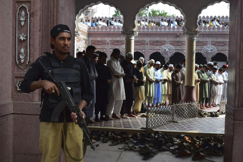 In this Thursday, Nov. 1, 2018, photo a police officer guards people offering prayers at Suneiri mosque in Peshawar, Pakistan. (AP Photo/Muhammad Sajjad)