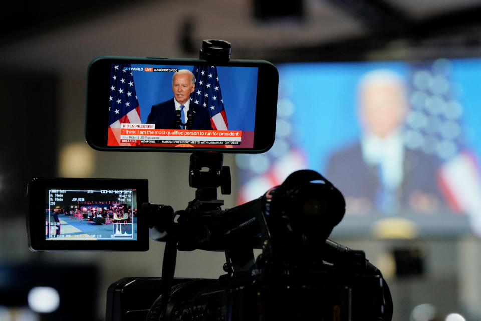 A mobile phone mounted on a camera shows President Biden next to two American flags.