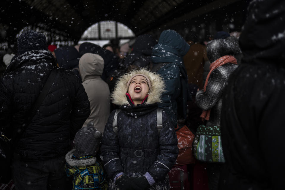 FILE - A girl catches snowflakes on her tongue as she waits with others to board a train to Poland, at Lviv railway station in Ukraine, Feb. 27, 2022, in Lviv, west Ukraine. (AP Photo/Bernat Armangue, File)