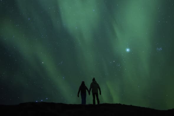 Northern lights (Aurora borealis) and silhouetted couple honeymoon