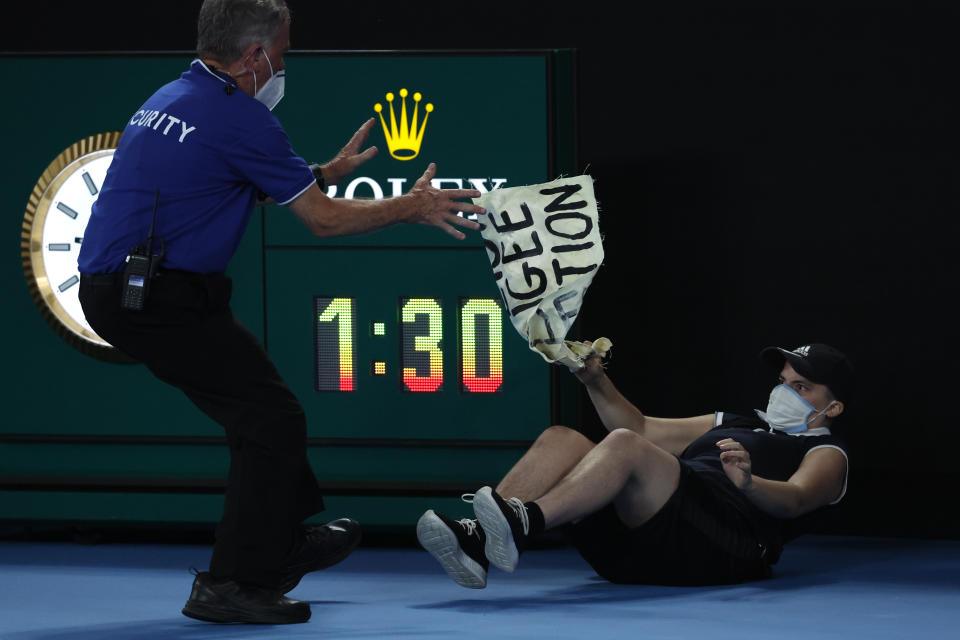 A security guard grapples with a protester who jumped onto Rod Laver Arena during the men's singles final at the Australian Open tennis championships in Melbourne, Australia, Sunday, Jan. 30, 2022. (AP Photo/Hamish Blair)