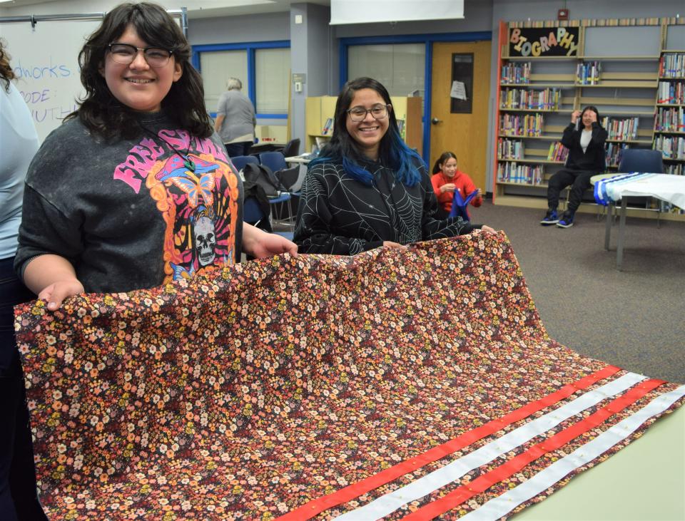 Kayden Ducheneaux (left), an eighth grader at Whittier Middle School, shows off her ribbon skirt-in-progress with volunteer Angela Heikkila (right) in the school library on Friday, April 21, 2023.