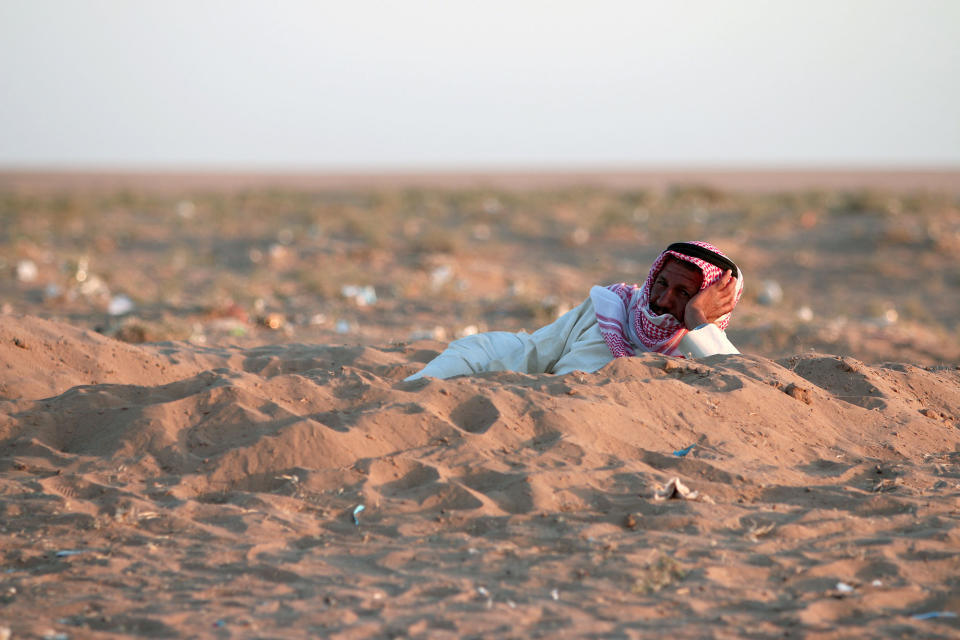 An Iraqi man lies in a hole dug in the sand upon reaching Syria