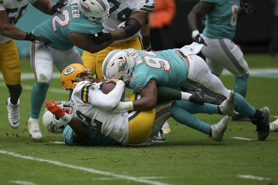 Green Bay Packers quarterback Aaron Rodgers (12) gets sacked by Miami Dolphins defensive tackle Christian Wilkins (94), and Miami Dolphins safety Eric Rowe (21), bottom, during the first half of an NFL football game, Sunday, Dec. 25, 2022, in Miami Gardens, Fla. (AP Photo/Jim Rassol)