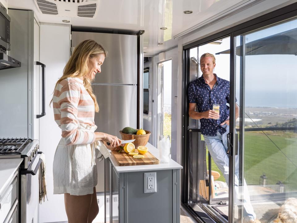 A person in the kitchen as another person stands by a doorway.