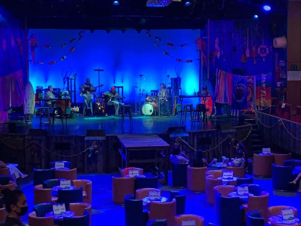 A stage for a Margaritaville show with blue lights and band performing to a large dining room.