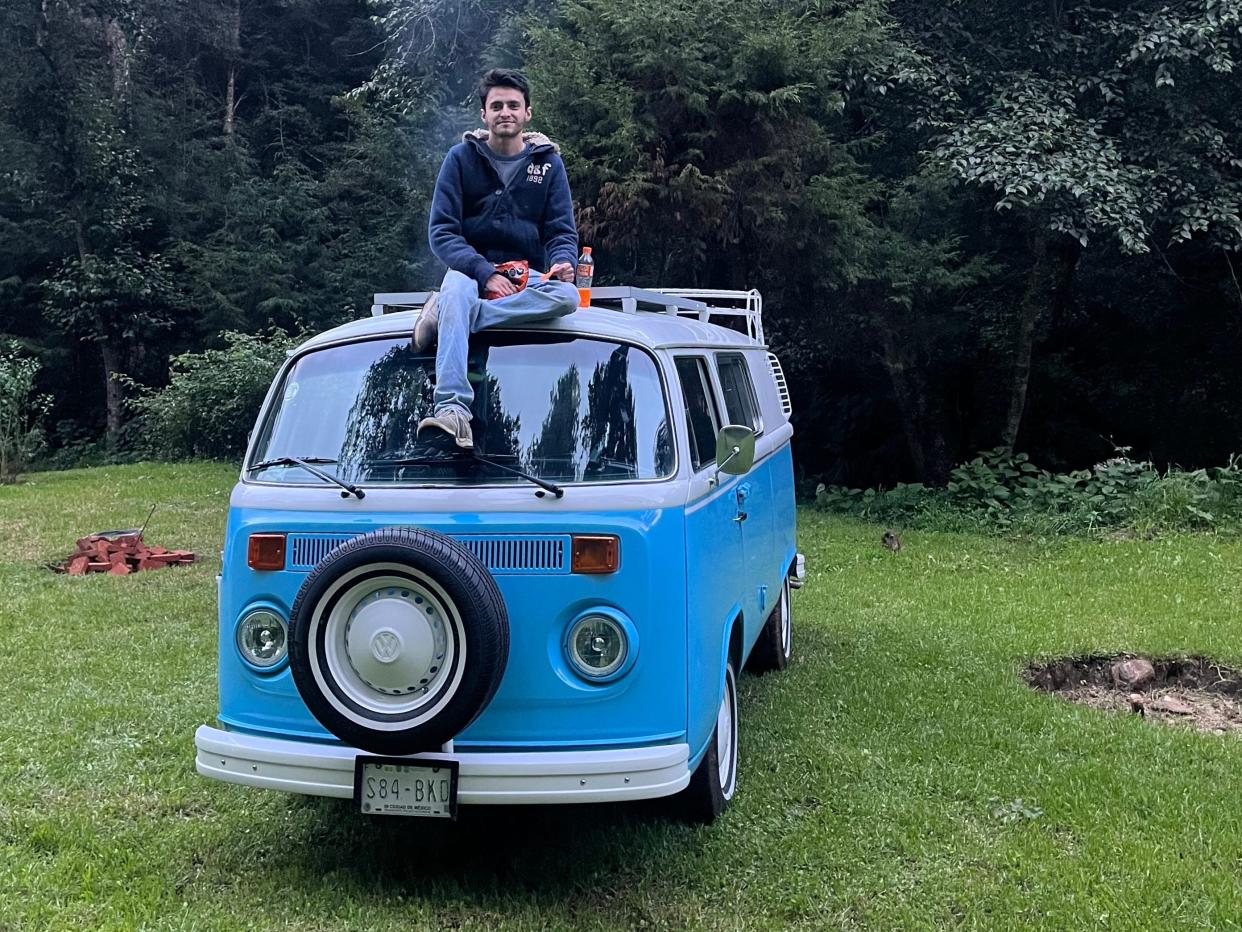 a man sits on top of a blue van in a grassy field