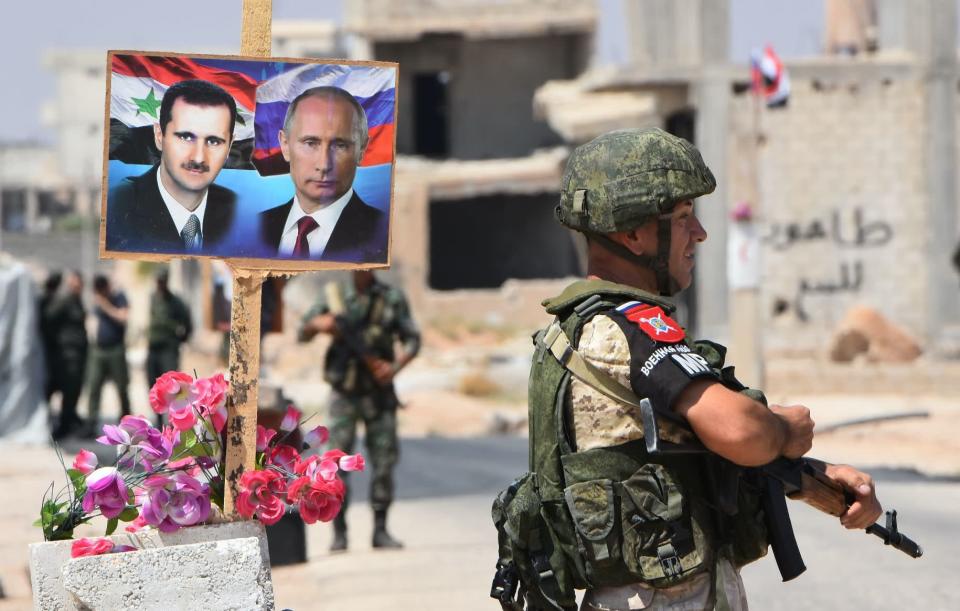 Members of Russian and Syrian forces stand guard near posters of Syrian President Bashar al-Assad and his Russian counterpart Vladimir Putin at the Abu Duhur crossing on the eastern edge of Idlib province on August 20, 2018. (Photo: GEORGE OURFALIAN/AFP/Getty Images)