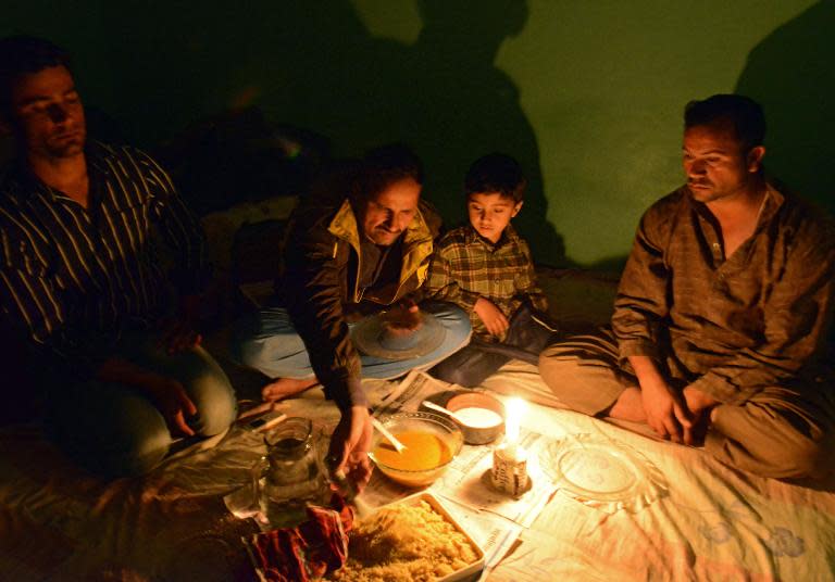 Pakistani refugee Nawid Ahmad (2nd L) and his family eat dinner by candlelight in their rented apartment in Kathmandu, on March 13, 2014