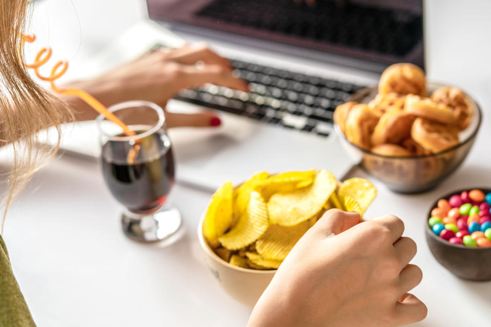 Woman eating snacks at her desk. (Getty Images)