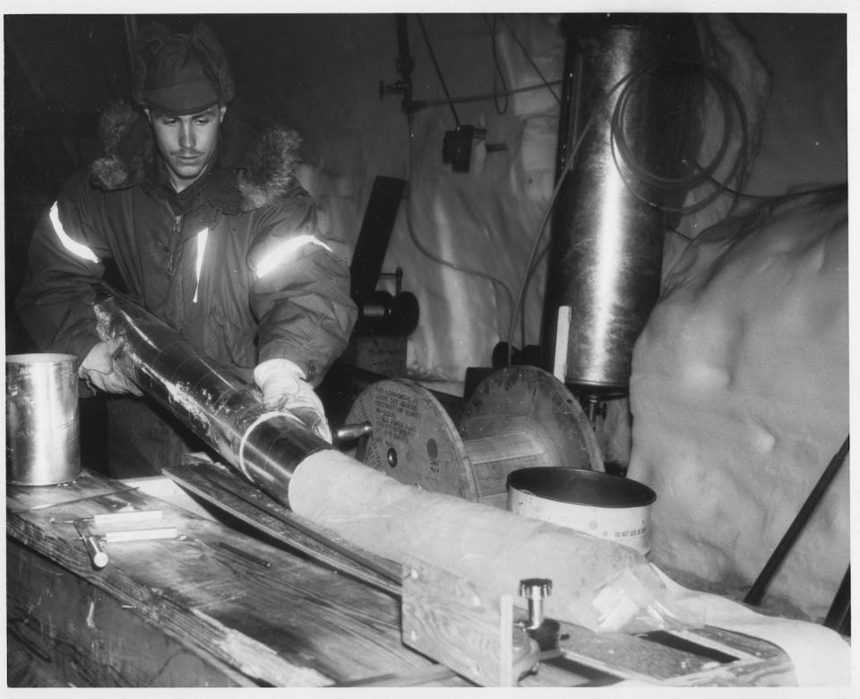 George Linkletter, working for the U.S. Army Corps of Engineers Cold Regions Research and Engineering Laboratory, examines a piece of ice core in the science trench at Camp Century. The base was shut down in 1967. U.S. Army Photograph