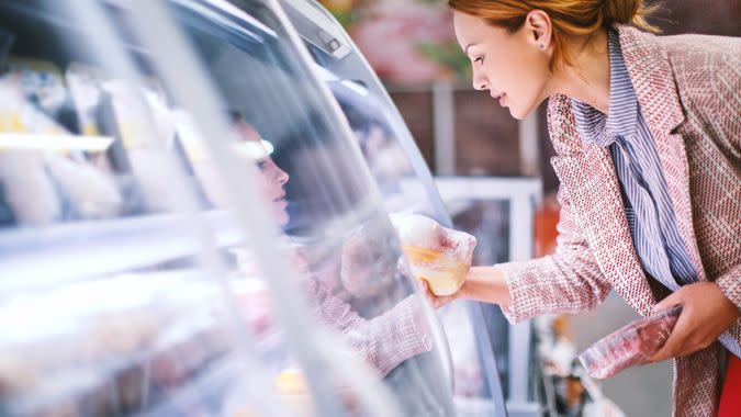 Attractive smiling brunette taking meat from a fridge at local supermarket.