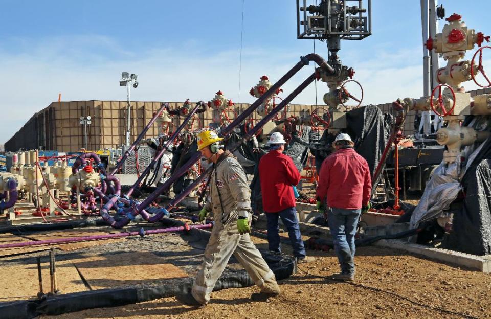 In this March 25, 2014 photo, Mike Hamilton, ground and crew supervisor for Bayou Well Services, walks past the well heads during a hydraulic fracturing operation at an Encana Corp. well pad near Mead, Colo. It takes a few weeks for the half dozen wells on a typical pad to be fracked, after which the petroleum products are extracted for years by operators like Encana. (AP Photo/Brennan Linsley)