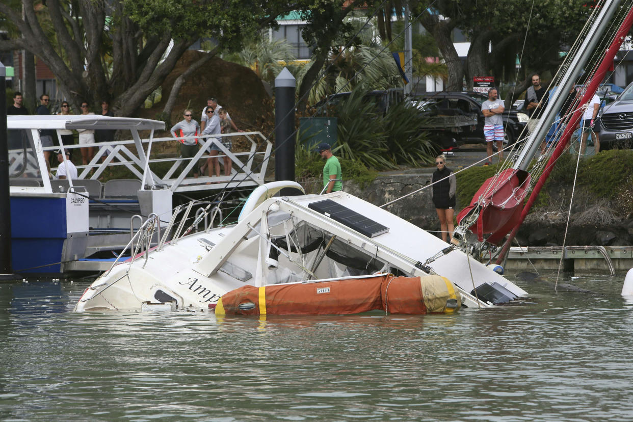 People look at a damaged boat in a marina at Tutukaka, New Zealand, Sunday, Jan. 16, 2022, after waves from a volcano eruption swept into the marina. An undersea volcano erupted in spectacular fashion Saturday near the Pacific nation of Tonga, sending tsunami waves crashing across the shore and people rushing to higher ground. (Tanya White/Northern Advcate/NZME via AP)