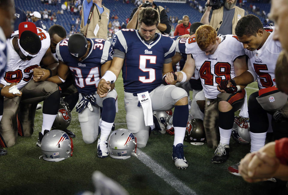 FILE - Tampa Bay Buccaneers defensive tackle Gerald McCoy (93), New England Patriots running back Shane Vereen (34), Patriots quarterback Tim Tebow (5), Buccaneers linebacker Joe Holland (49) and Buccaneers quarterback Josh Freeman (5) kneel an pray with others at midfield after an NFL preseason football game Friday, Aug. 16, 2013, in Foxborough, Mass. Public display of faith is nothing new in football or sports.(AP Photo/Michael Dwyer, File)