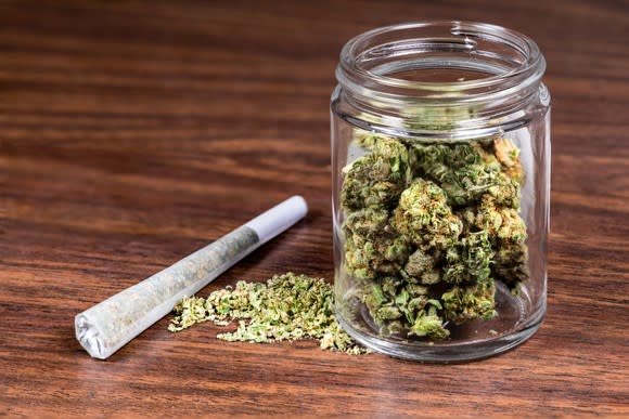 Jar of dried cannabis with seeds and papers on a wood table.