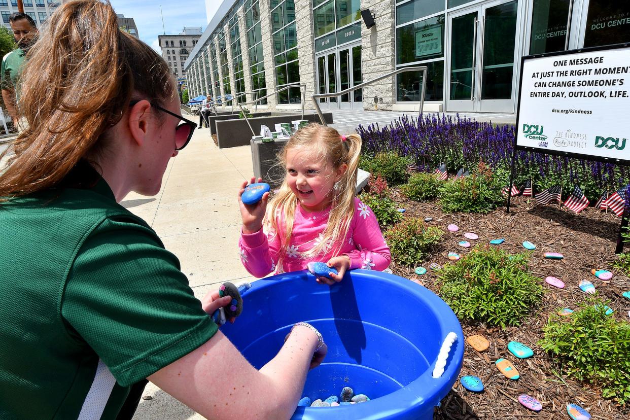 Autumn Birkbeck, 5, of Paxton shows a rock that says "smile" to Digital Federal Credit Union (DCU) marketing communications intern Cayla Wade as the financial and realty company installs its Kindness Rocks Garden outside the DCU Center Friday ahead of city’s Tercentennial Celebration. Autumn is the daughter of Robert Birkbeck, left corner, who's a member of the DCU marketing department.